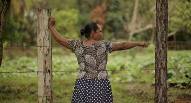 Frau steht an Stacheldrahtzaun.