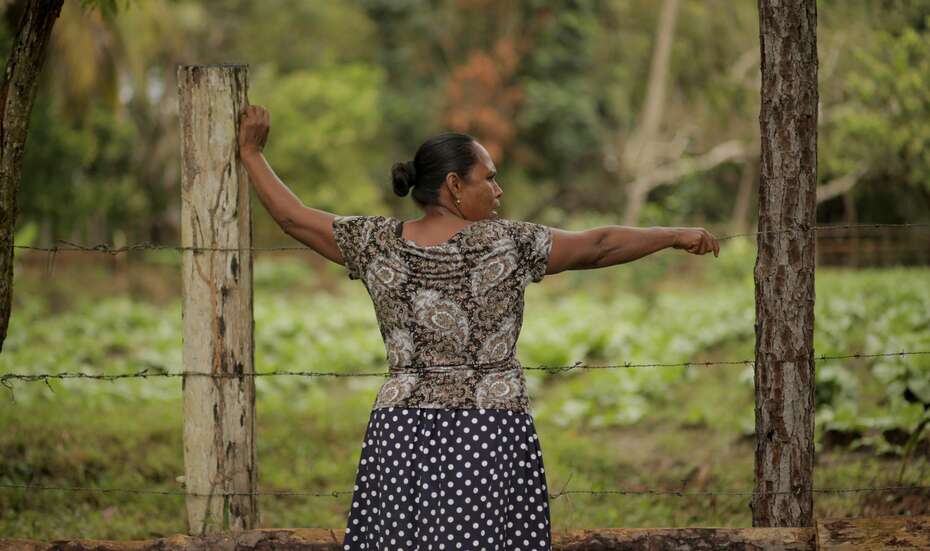 Frau steht an Stacheldrahtzaun.