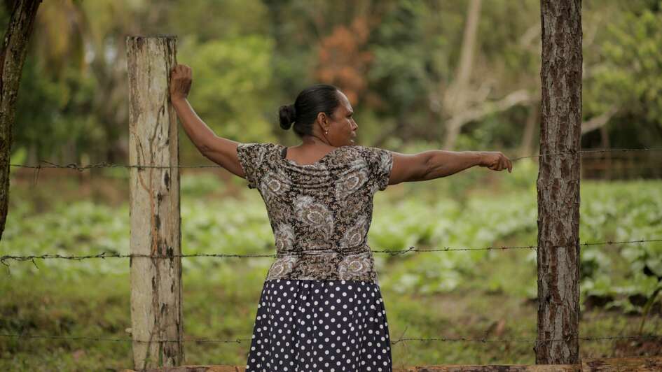 Frau steht an Stacheldrahtzaun.