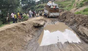 Eine Straße mit einem riesigen Schlagloch voller Wasser. Ein Transporter hat Schwierigkeiten, fort zu kommen.