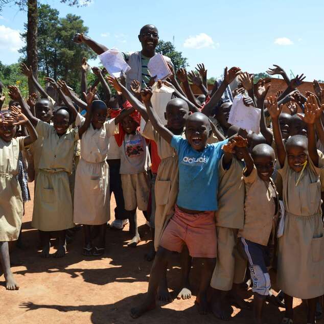 Eine Gruppe jubelnder Kinder steht mit ihrem Lehrer vor ihrer Grundschule.