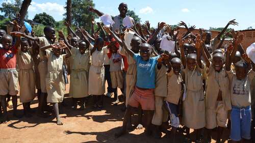 Hilfe für Burkina Faso - Bild: Eine Gruppe jubelnder Schulkinder steht mit ihrem Lehrer vor einer Schule.