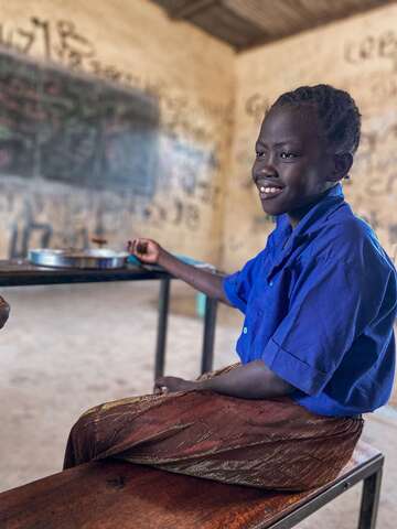 Ein Kind sitzt im Klassenraum auf einer Schulbank und hat etwas zu Essen