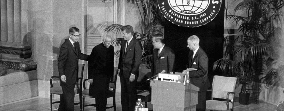 Schwarzweiß-Foto der fünf Männer, im Hintergrund hängt ein Schild "World Food Congress"