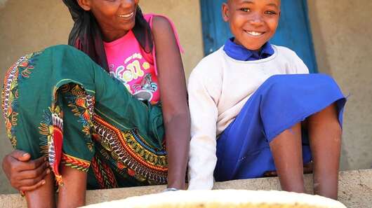 Eine Frau und ein Mädchen sitzen auf einer Treppe, vor ihnen ein flacher Korb.