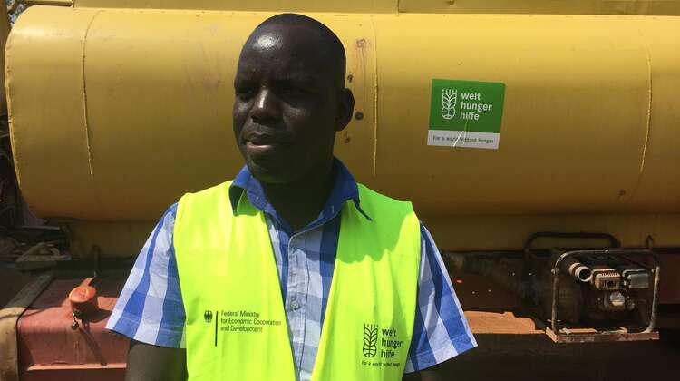 Tankwagen gefüllt mit Wasser, davor steht ein Welthungerhilfemitarbeiter.