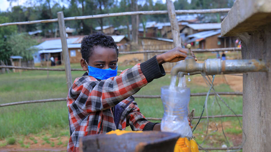 Ein Junge mit einem Mundschutz holt Wasser aus einem Brunnen.