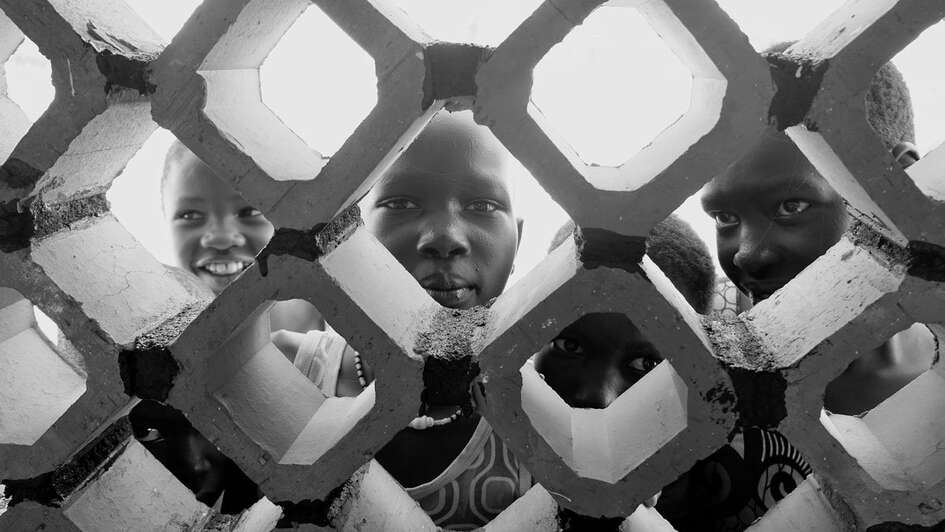 Kinder blicken durch Löcher in einer Mauer.