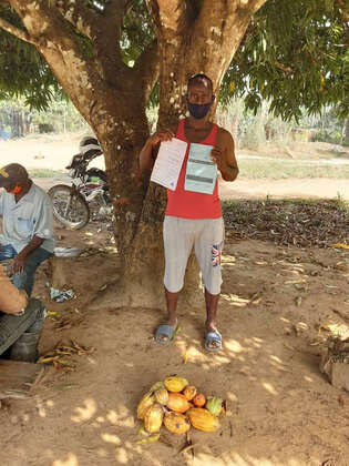 Ein Man steht vor geernteten Kakofrüchten und hält ein Zertifikat in der Hand.
