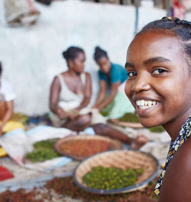Mädchen und Frauen arbeiten in einer Pfefferfabrik, ein Mädchen im Vordergrund lächelt in die Kamera