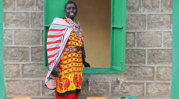 Eine Frau steht an einem grünen Fenster und lacht in die Kamera.