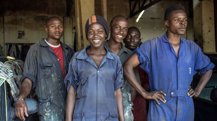 Eine Gruppe junger Menschen in blauen Arbeitsanzügen schauen lächelnd in die Kamera