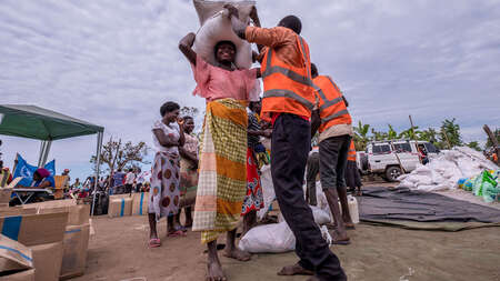 Eine Frau bekommt von einem Mann in Sicherheitsweste Säcke und Pakete.