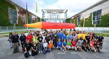 Gruppenfoto von demonstrierenden Personen von verschiedenen Hilfsorganisationen. Im Hintergrund das Kanzleramt und ein großer aufblasbarer Rotstift.