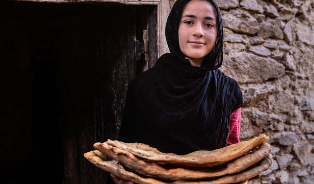 Eine Frau hält Fladenbrot und lächelt in die Kamera.