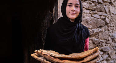Eine Frau hält Fladenbrot und lächelt in die Kamera.