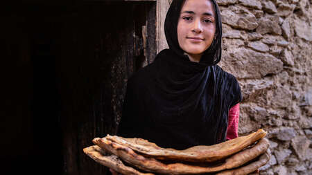 Eine Frau hält Fladenbrot und lächelt in die Kamera.