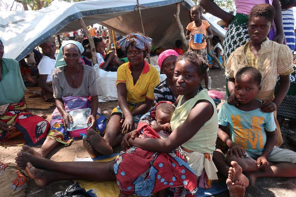 Drei Frauen und fünf Kinder sitzen vor einer Plane, die als Notunterkunft aufgespannt wurde.