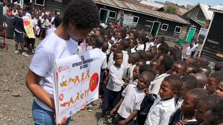 Eine Frau zeigt Schulkindern in der Nähe von Goma (D. R. Kongo) zur Ebola-Prävention Bilder, wie sie sich gründlich die Hände waschen können.
