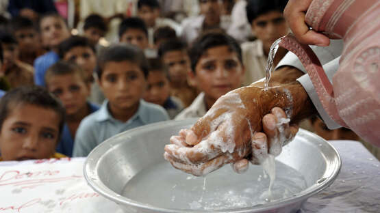 Hände voller Schaum über einer Schüssel. Im Hintergrund sieht man Kinder, die zuschauen.