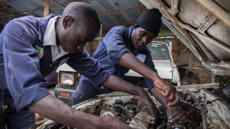 Zwei Männer schrauben am Motor eines Autos unter geöffneter Motorhaube.