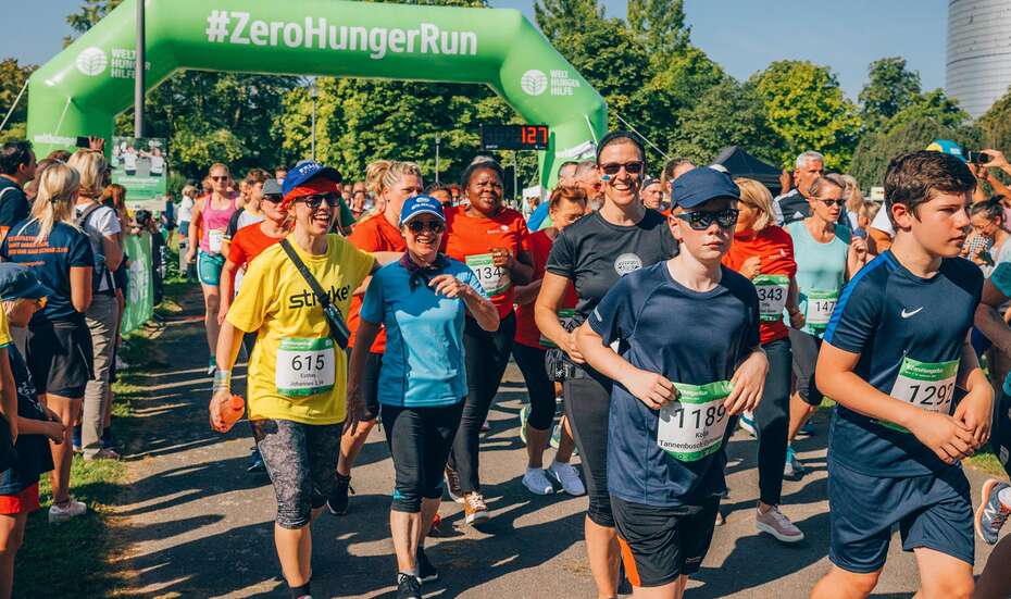 Dicht gedrängt laufen Menschen in Sportkleidung unter einem Tor mit der Aufschrift #ZeroHungerRun durch