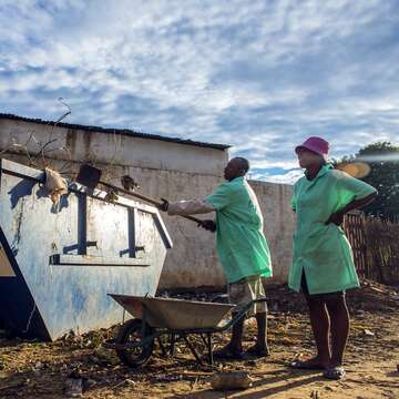 Zwei Männer schaufeln Müll in einen Container
