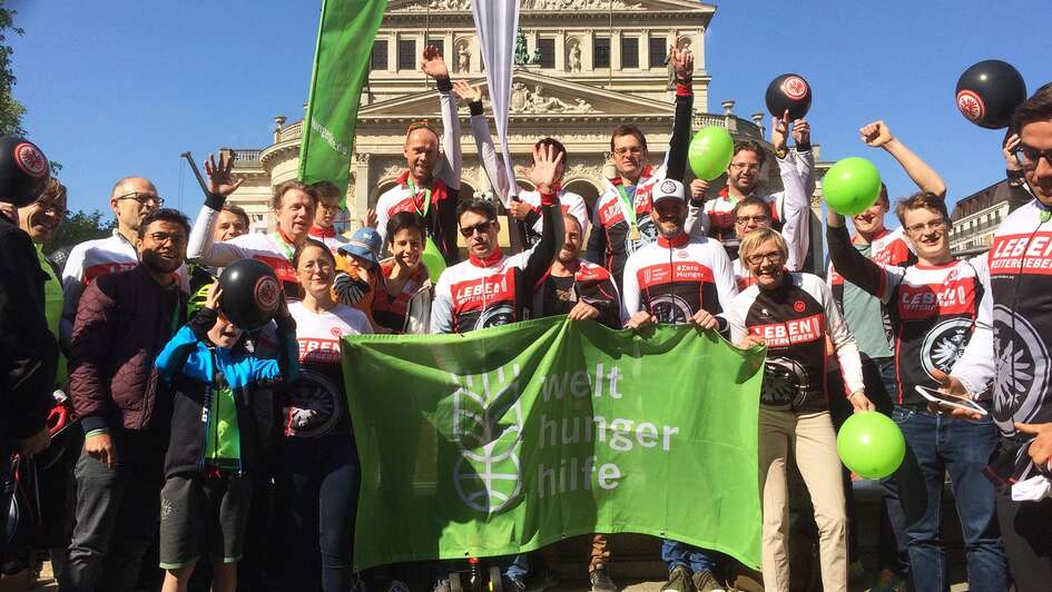 Eine Gruppe von Menschen mit Welthungerhilfe-Flagge schaut lachend in die Kamera.