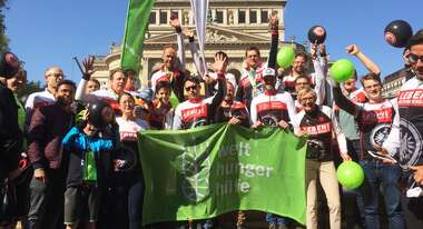 Eine Gruppe von Menschen mit Welthungerhilfe-Flagge schaut lachend in die Kamera.