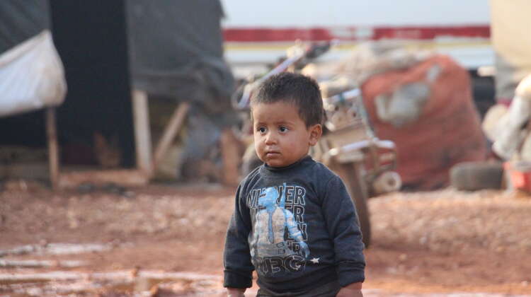 Ein kleiner Junge geht durch den Matsch, im Hintergrund sind Notunterkünfte zu sehen