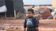 Ein kleiner Junge geht durch den Matsch, im Hintergrund sind Notunterkünfte zu sehen