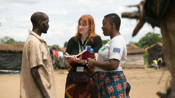 Zwei Frauen unterhalten sich mit einem Mann, eine hält ein Notizbuch in der Hand.