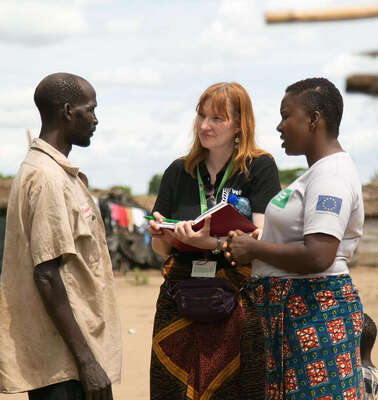 Zwei Frauen unterhalten sich mit einem Mann, eine hält ein Notizbuch in der Hand.