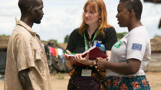 Zwei Frauen unterhalten sich mit einem Mann, eine hält ein Notizbuch in der Hand.