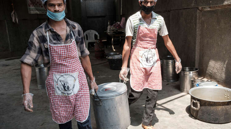 Zwei Männer mit Schürze tragen einen großen Topf.