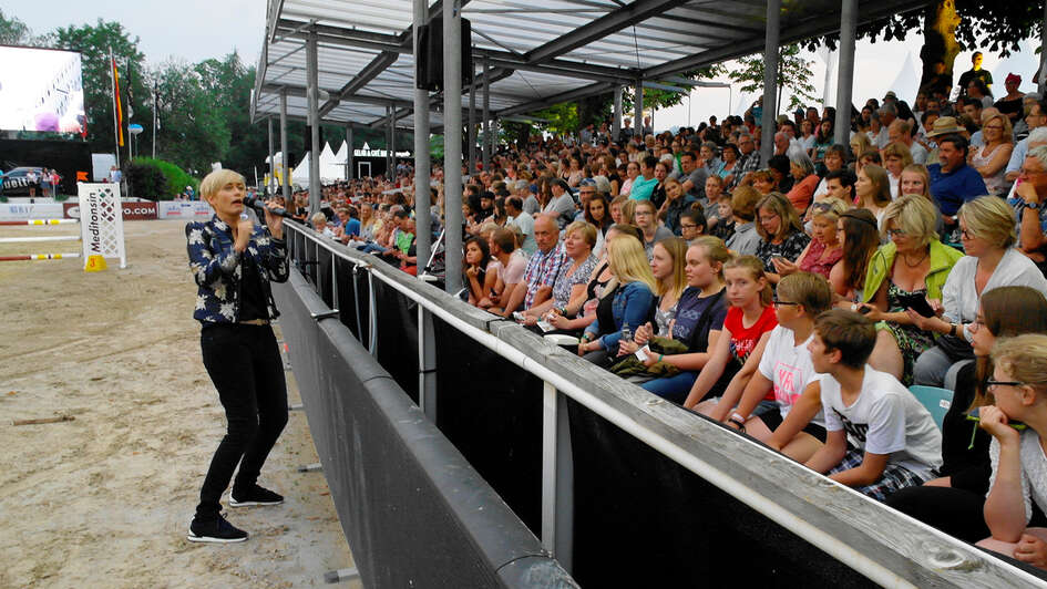 Die Schauspielerin Gesine Cukrowski steht auf einem Reitplatz und moderiert die SMS-Spendenaktion vor vielen Zuschauern.