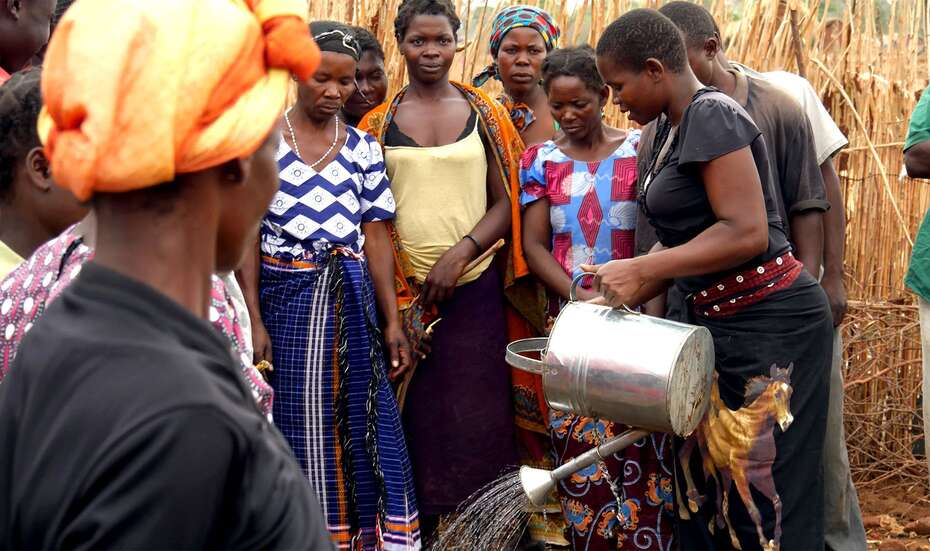 Eine Gruppe von Menschen ist um Annie versammelt. Annie hält eine Gießkanne