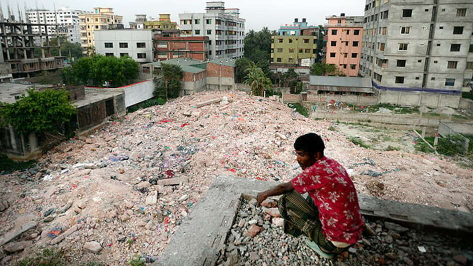 Ein Mann sitzt in der Hocke und schaut auf die Trümmer eines Gebäudes