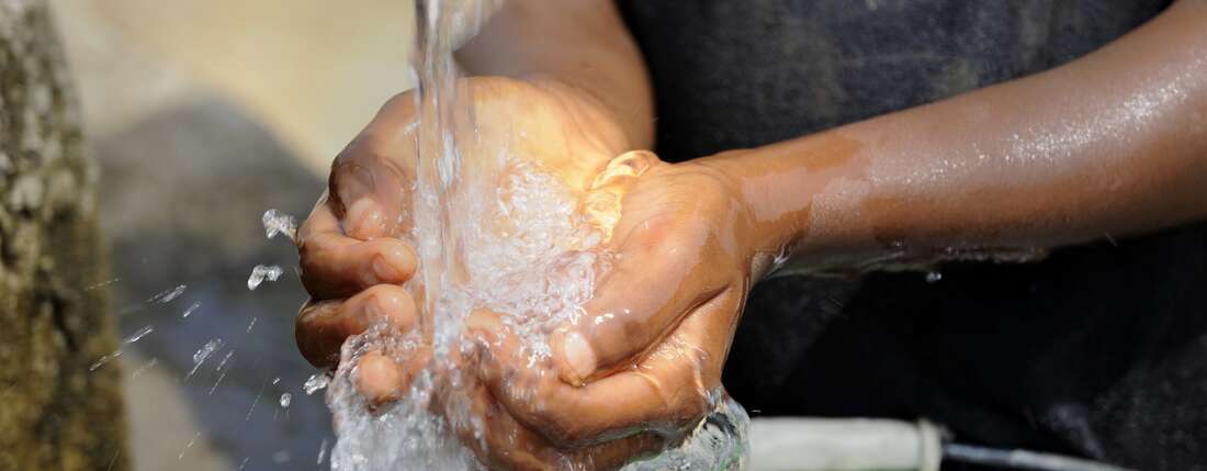 Zugang zu Wasser: Hände schöpfen Wasser unter einem Wasserstrahl.