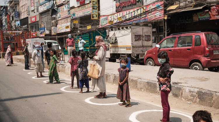 Mehrere Menschen stehen in einer Schlange. Auf dem Boden sind aufgemalte weiße Kreise.
