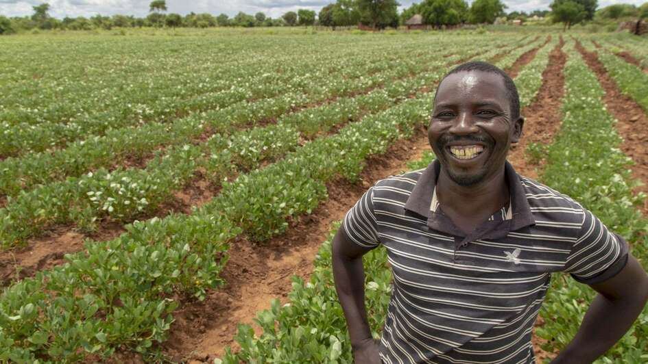 Entwicklungszusammenarbeit: Ein Mann steht lächelnd vor einem Feld mit langen Pflanzenreihen.