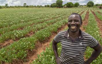 Ein Mann steht lächelnd vor einem Feld mit langen Pflanzenreihen.