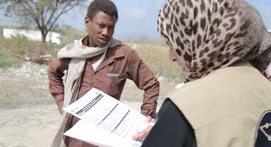Eine Frau und ein Mann sprechen miteinander. Die Frau hat Papiere in der Hand.