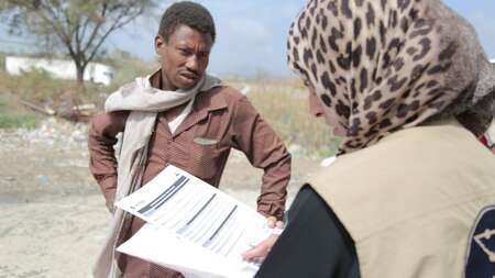 Eine Frau und ein Mann sprechen miteinander. Die Frau hat Papiere in der Hand.