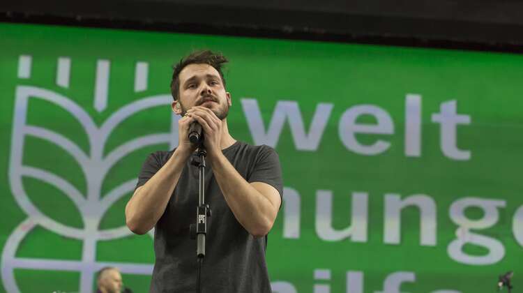 2018-robert-redweik-konzert-david-klammer.jpg Robert Redweik auf der Bühne, im Hintergrund das Welthungerhile-Logo.