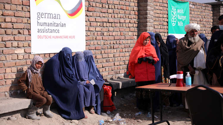 2022-afghanistan-hires-verteilung-banner_C_parwiz-sabawoon-welthungerhilfe.jpg Verschleierte Frauen warten bei einer Lebensmittelverteilung. Im Hintergrund sind Banner mit Welthungerhilfe-Logo und von German Humanitarian Assisstance zu sehen.