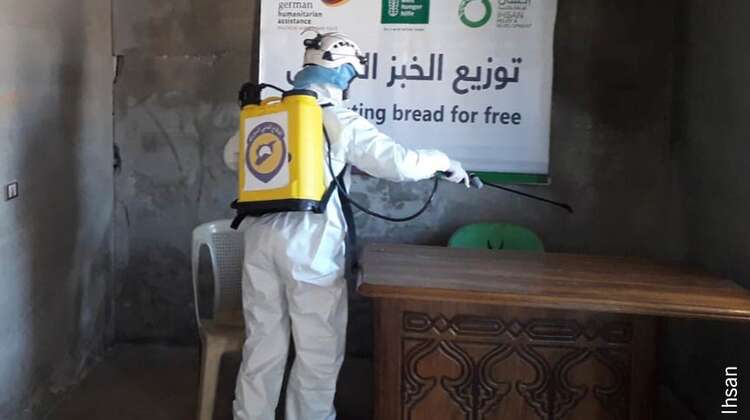 Eine Person in Schutzkleidung desinfiziert eine Verteilstätte für Brot