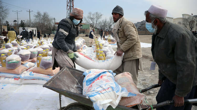 2022-afghanistan-hires-verteilung-lebensmittel-sack-mit-mehl.JPG Zwei Männer laden einen Sack Mehl auf eine Schubkarre.