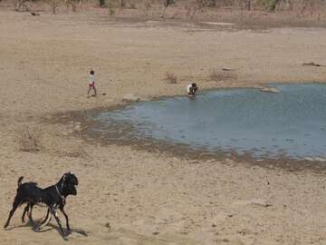 EIne Person sitzt an einer Wasserlache eines fast ausgetrockneten Sees.
