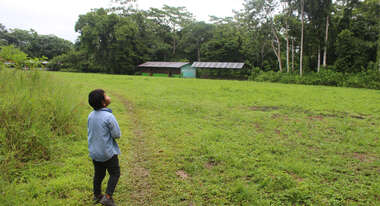 Ein Kind steht auf einer großen Wiese vor einem Haus, Peru 2022.